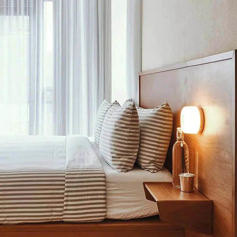Nordic LED wall sconce on a wooden headboard in a bedroom, white metal with a warm glow.