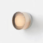 LED Wall Sconce on white wall; amber ribbed glass globe, minimalist metal backplate.