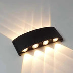 A curved black wall-mounted light fixture with four illuminated bulbs, casting warm light beams onto a light-colored wall.