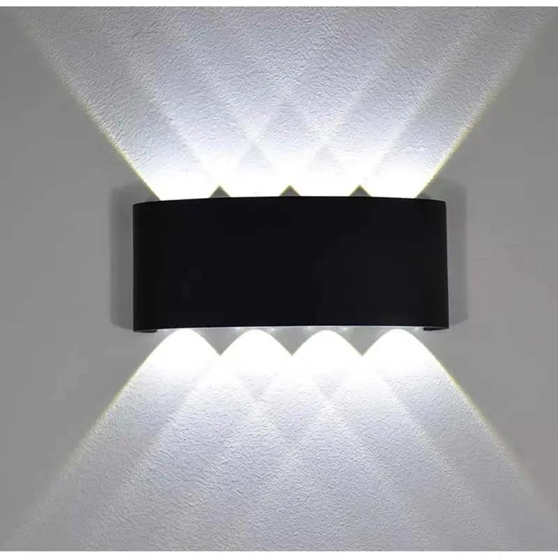 A modern black wall-mounted light fixture with three upward-facing and three downward-facing illuminated beams, shown against a textured white wall.