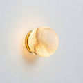 Wall-mounted light fixture with a gold frame and beige glass shade on a light gray background
