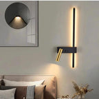 Wall lights: vertical LED strip with brass adjustable reading arm on a dark wall sconce above a bed in bedroom.