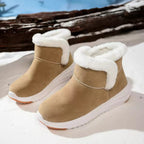A pair of beige ankle-height winter boots with white faux-fur trim and white soles, photographed outdoors on a snowy surface with a log in the background.