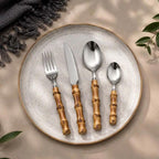 24-Piece Bamboo Handle Cutlery Set on a speckled ceramic plate; four bamboo-handled stainless steel utensils.