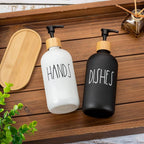 Two soap dispensers labeled 'HANDS' and 'DISHES' on a wooden surface with a wooden tray and plant in the background.