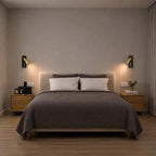A modern bedroom scene featuring a bed dressed in a textured dark gray quilt and white pillows, flanked by two matching wooden nightstands and black wall sconces against a warm gray wall.
