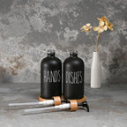 Black 'HANDS' and 'DISHES' bottles with a white vase with flowers on a textured gray background